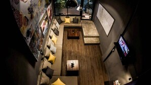 A modern living room with a sofa, cushions, a coffee table, a map on the wall, and a television. - In A Box Hostel (Bangkok)