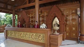 A reception area with a wooden counter, ornate carvings, and a large vase.