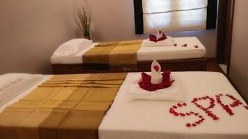 Una habitación de hotel con dos camas, cada una con una colcha blanca y una vela roja. La palabra "SPA" está escrita con puntos rojos sobre la cama en primer plano.