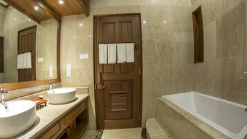 A bathroom with two sinks, a bathtub, and a wooden door with towels hanging on it.