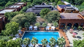 An aerial view of a resort with a central swimming pool surrounded by lounge chairs and umbrellas, a courtyard with a wooden deck, and traditional-style buildings. - Heritage Bagan Hotel (Nyaung-U)