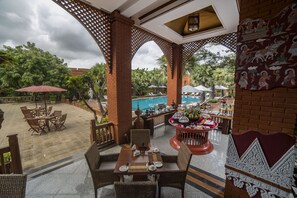 Un espacio exterior para comer con mobiliario de mimbre, piscina y una pared decorativa.
