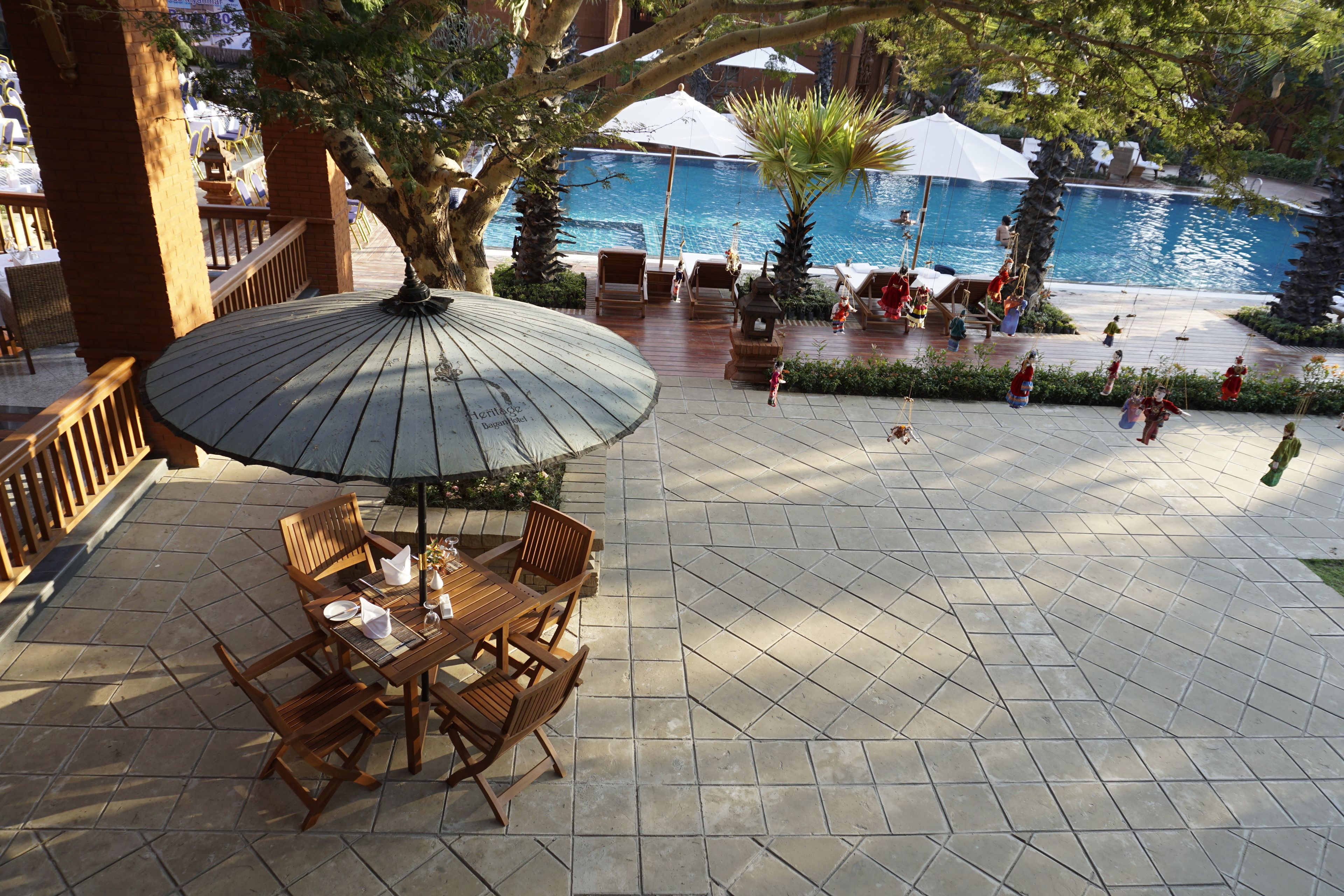 An outdoor patio with a table and chairs, a pool, and umbrellas.