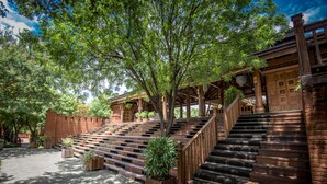 A wooden staircase leading up to a building with a covered porch area, surrounded by trees and potted plants.