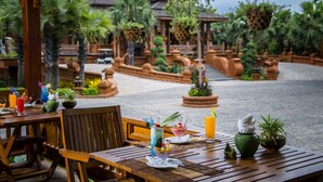 An outdoor dining area with wooden tables and chairs, potted plants, and hanging planters.