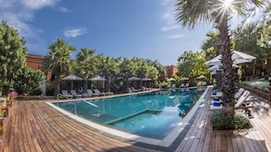 A pool area with a wooden deck, lounge chairs, umbrellas, and palm trees.