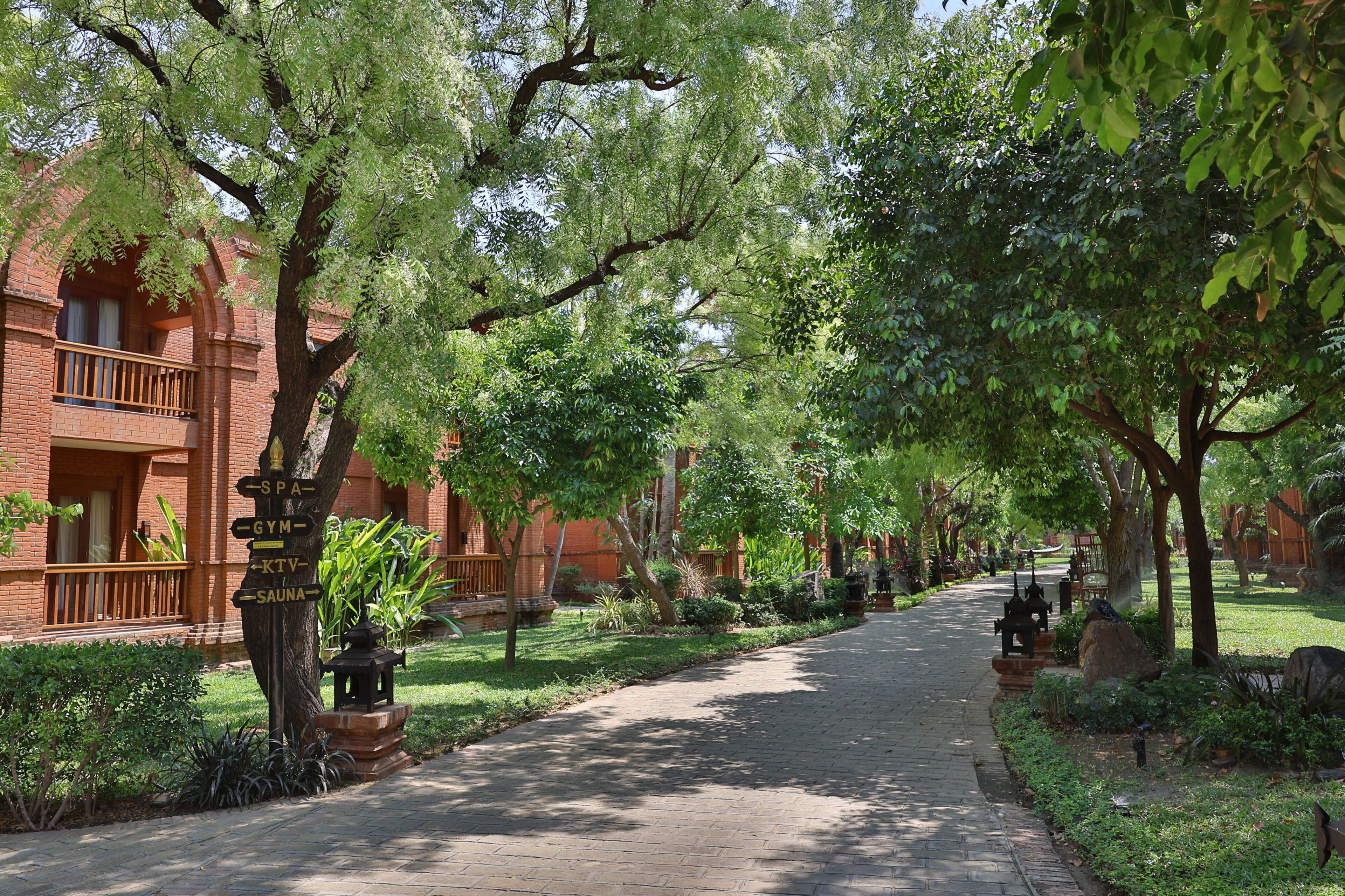 A brick building with a balcony, a paved walkway, and lush greenery.