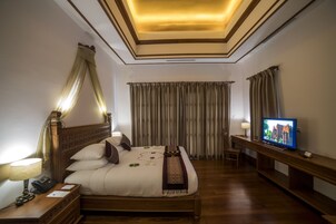 Una habitación de hotel con una cama grande, lámparas de noche, televisión y cortinas.