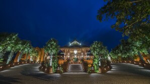 A grand entrance with a staircase leading to a building, surrounded by palm trees and well-lit pathways.