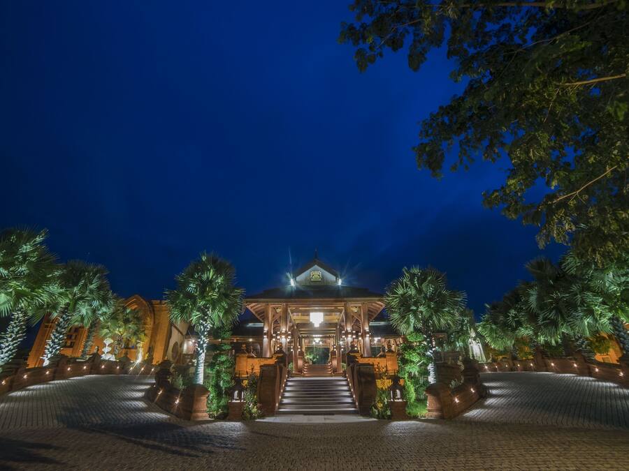 A grand entrance with a staircase leading to a building, surrounded by palm trees and well-lit pathways.