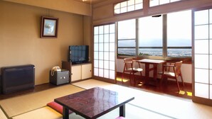 A traditional Japanese room with tatami flooring, a low table, a TV, a safe, and a view of a cityscape through large windows. - Yakushidaira Akanejyuku (Matsumoto)