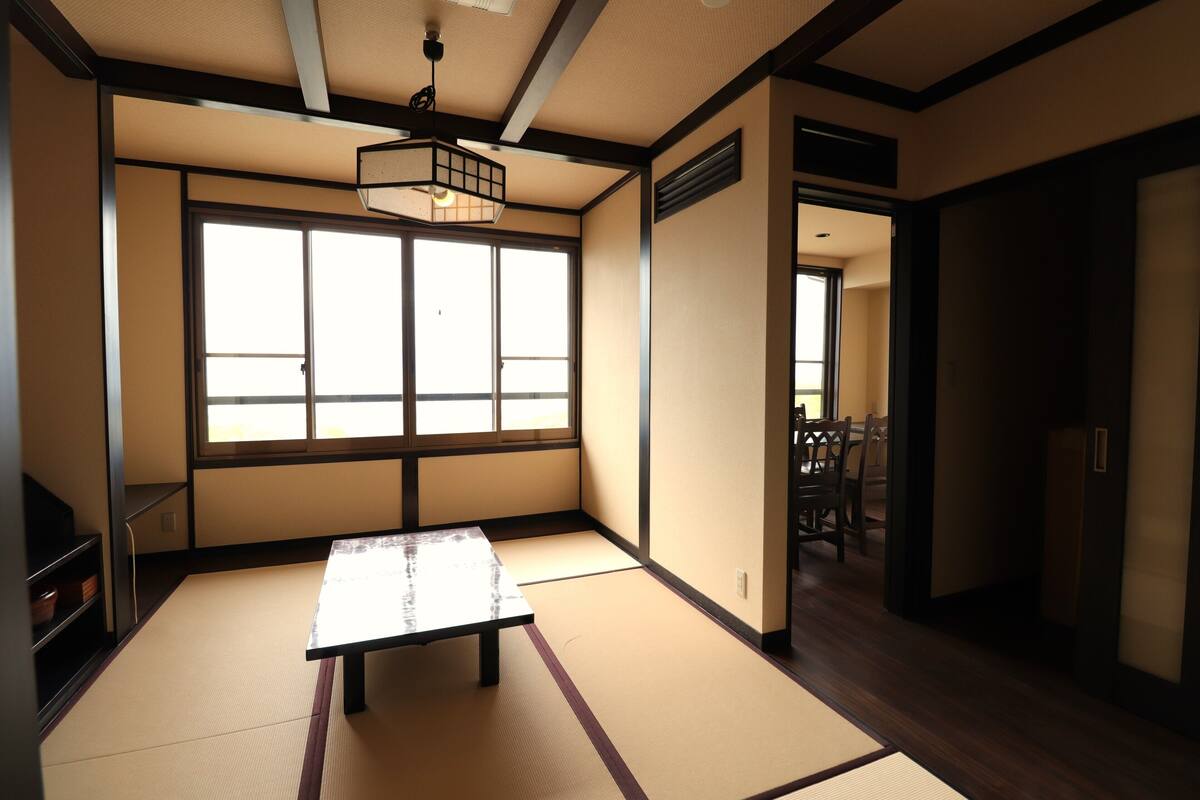 A traditional Japanese room with tatami flooring, a low table, and a sliding door leading to another room.