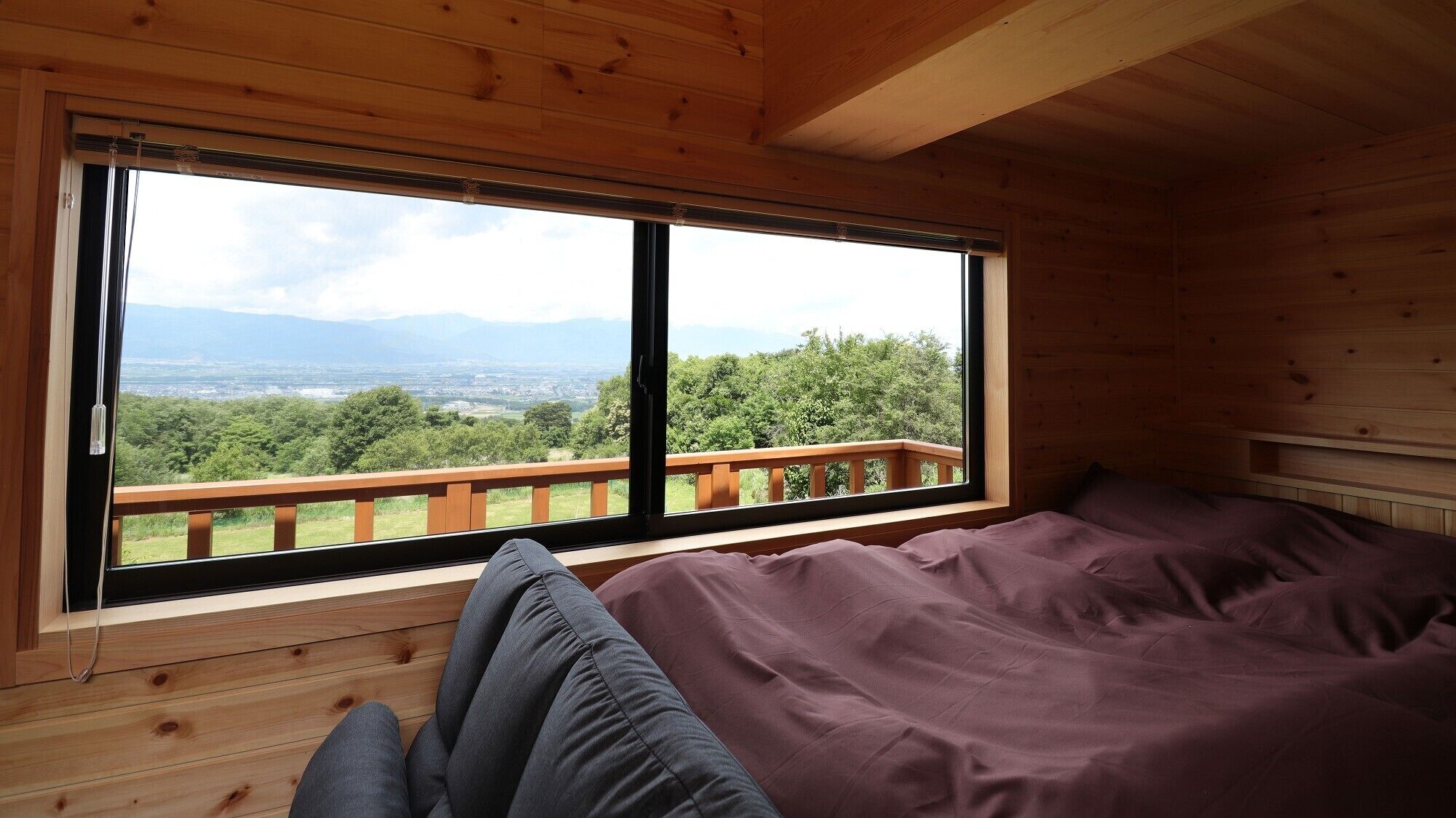 Ein Holzhütten-Zimmer mit großem Fenster, einem Bett und Blick auf Wald und Berge.