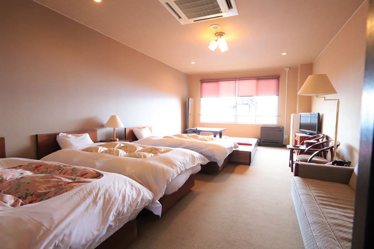 A hotel room with two beds, a desk, a chair, a television, and a window with blinds.