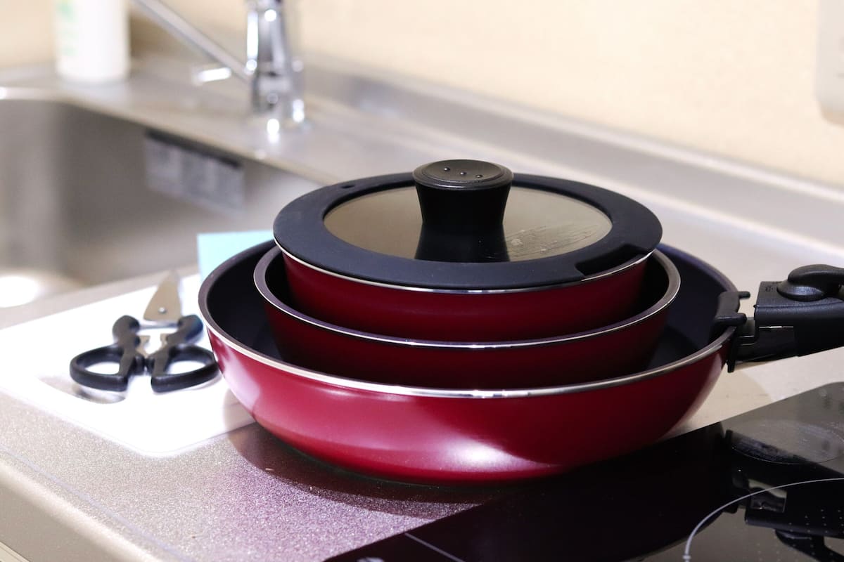 A red pot on a stove with a lid, a pair of scissors, and a faucet in the background.