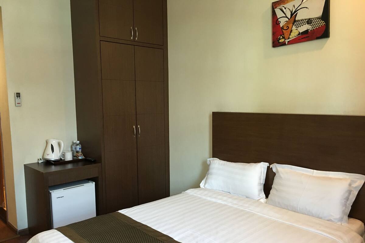 Une chambre d’hôtel équipée d’un lit, d’une table de chevet, d’une machine à café, d’une bouteille d’eau et d’un petit réfrigérateur.