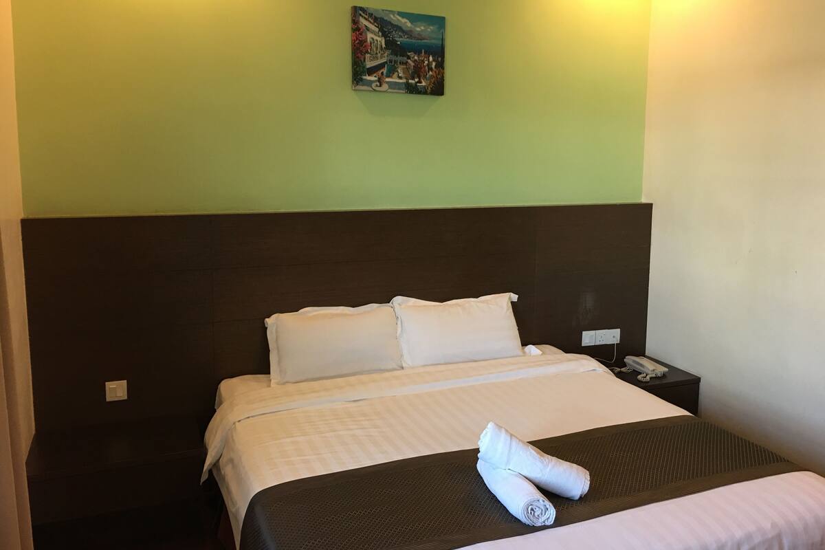 Une chambre d’hôtel avec un lit, des oreillers, une serviette pliée, une table de chevet avec un téléphone et un tableau au mur.