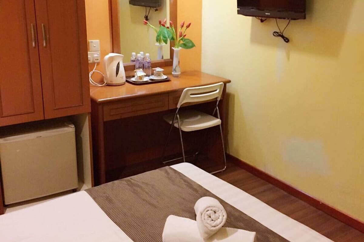 A hotel room with a bed, a desk, a chair, a mirror, a television, and a small refrigerator.
