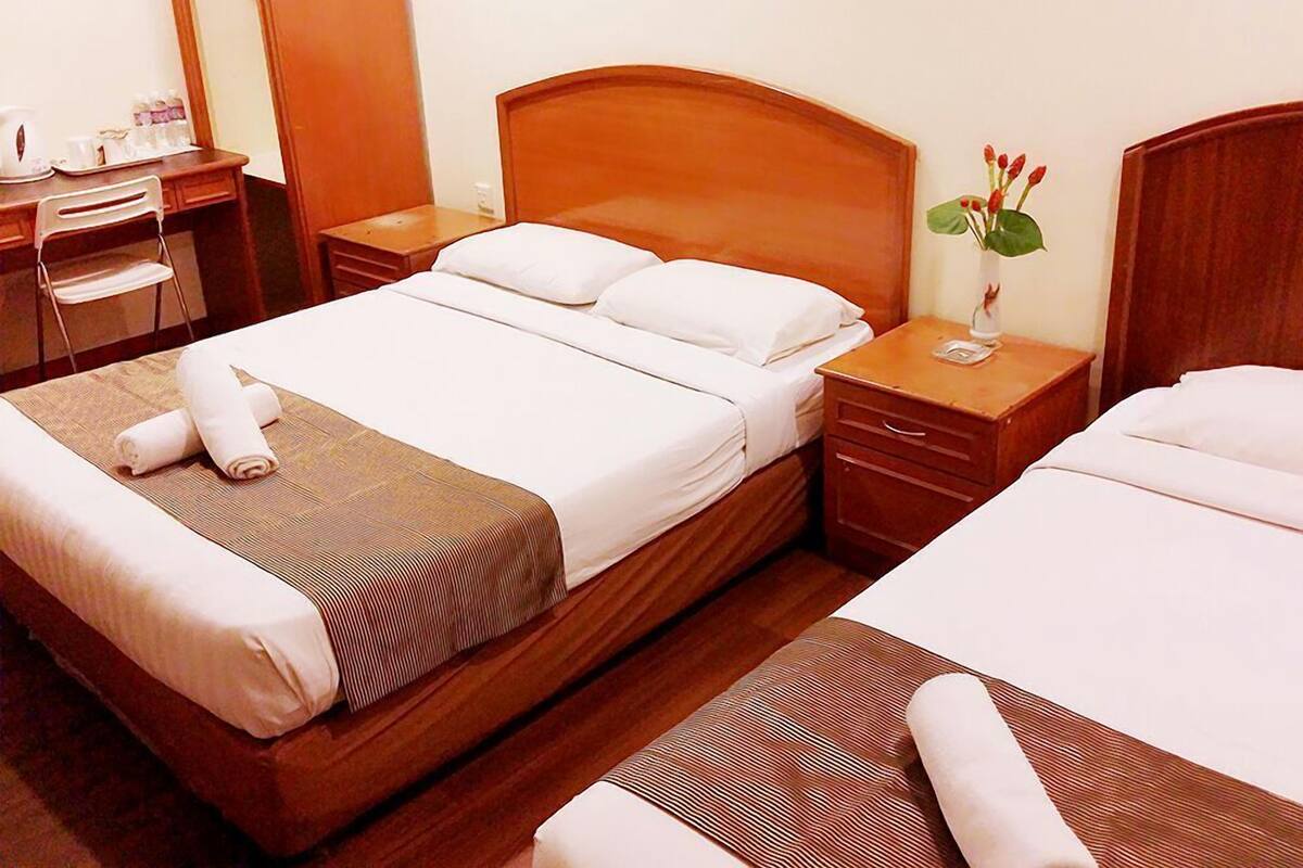 A hotel room with a double bed, a desk with a chair, a bedside table with a vase of flowers, and a wooden headboard.