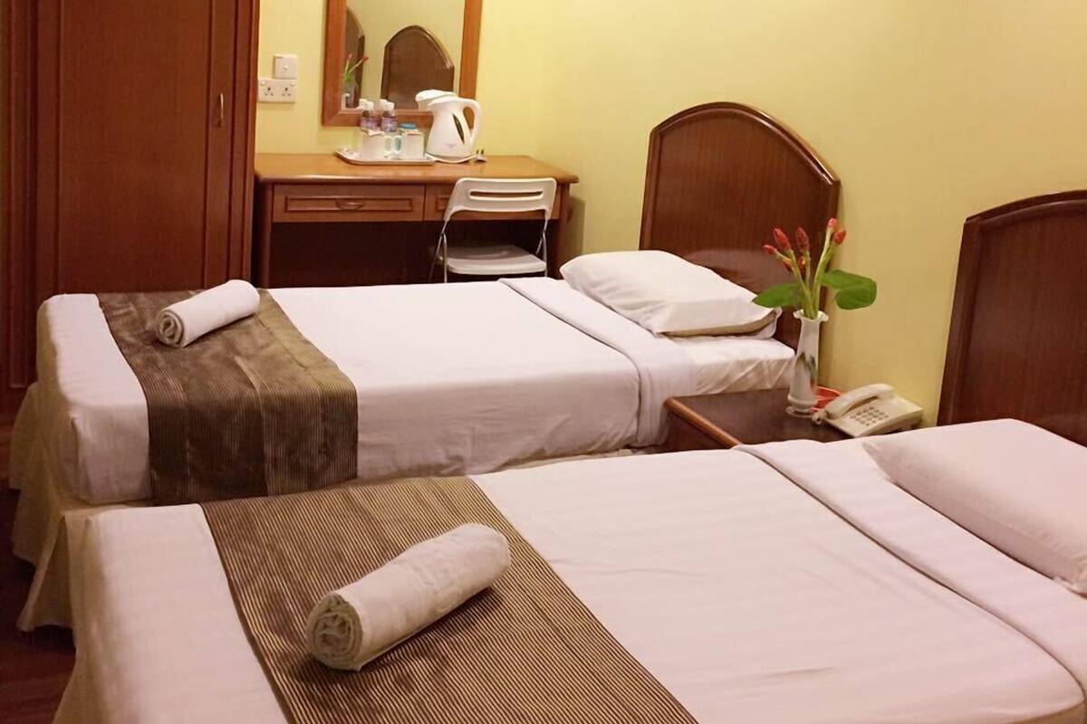 A hotel room with two beds, a wooden wardrobe, a desk with a mirror, a telephone, and a vase with flowers.