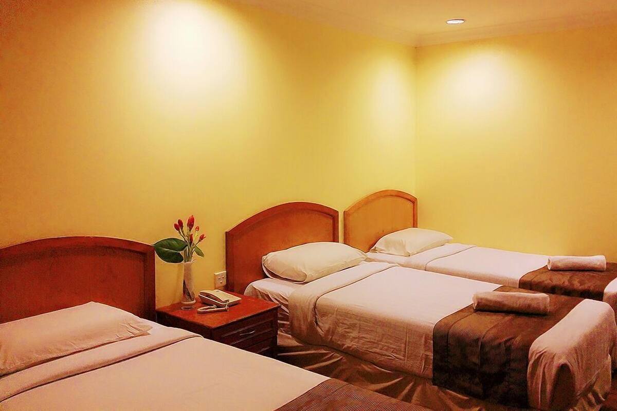 A hotel room with two single beds, a nightstand with a vase of flowers, and a small table with a book and a pen.