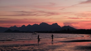 A beach scene with mountains in the background during sunset. - Pranburi Delight Resort (Sam Roi Yot)