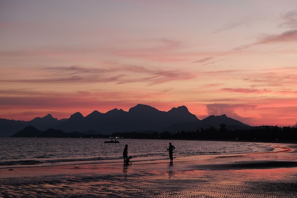 A beach scene with mountains in the background during sunset.