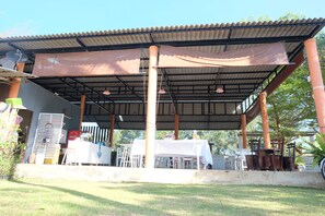Un espacio al aire libre cubierto con mesas y sillas, un mantel blanco y un refrigerador de Coca-Cola.
