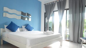 A bedroom with a white bed, blue pillows, a white bench, and a large window with curtains. - Pranburi Delight Resort (Sam Roi Yot)