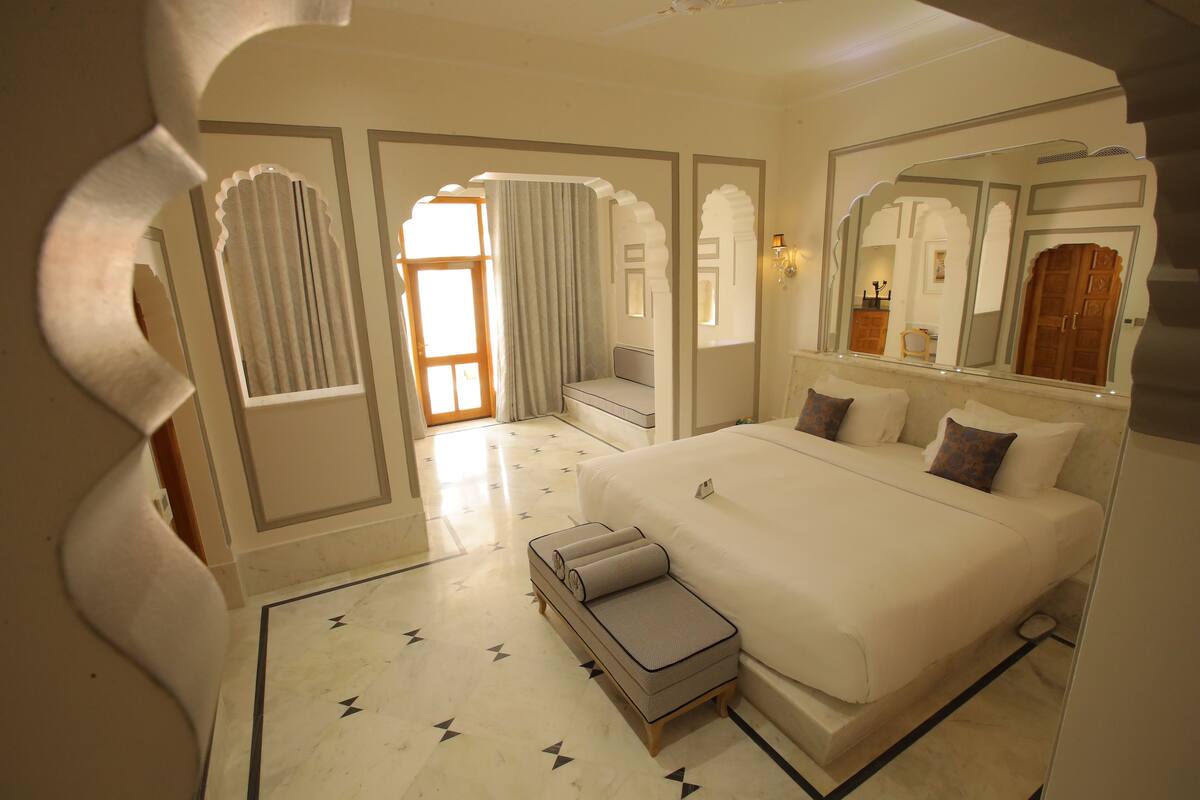 Une chambre spacieuse avec un grand lit, un coin salon avec un canapé et des rideaux, et un miroir décoratif.