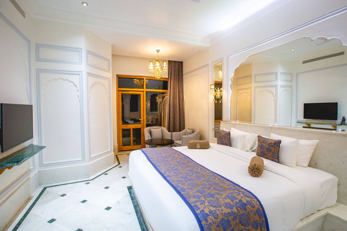 Une chambre d’hôtel avec un grand lit, une télévision, un coin salon avec des fauteuils et un miroir.