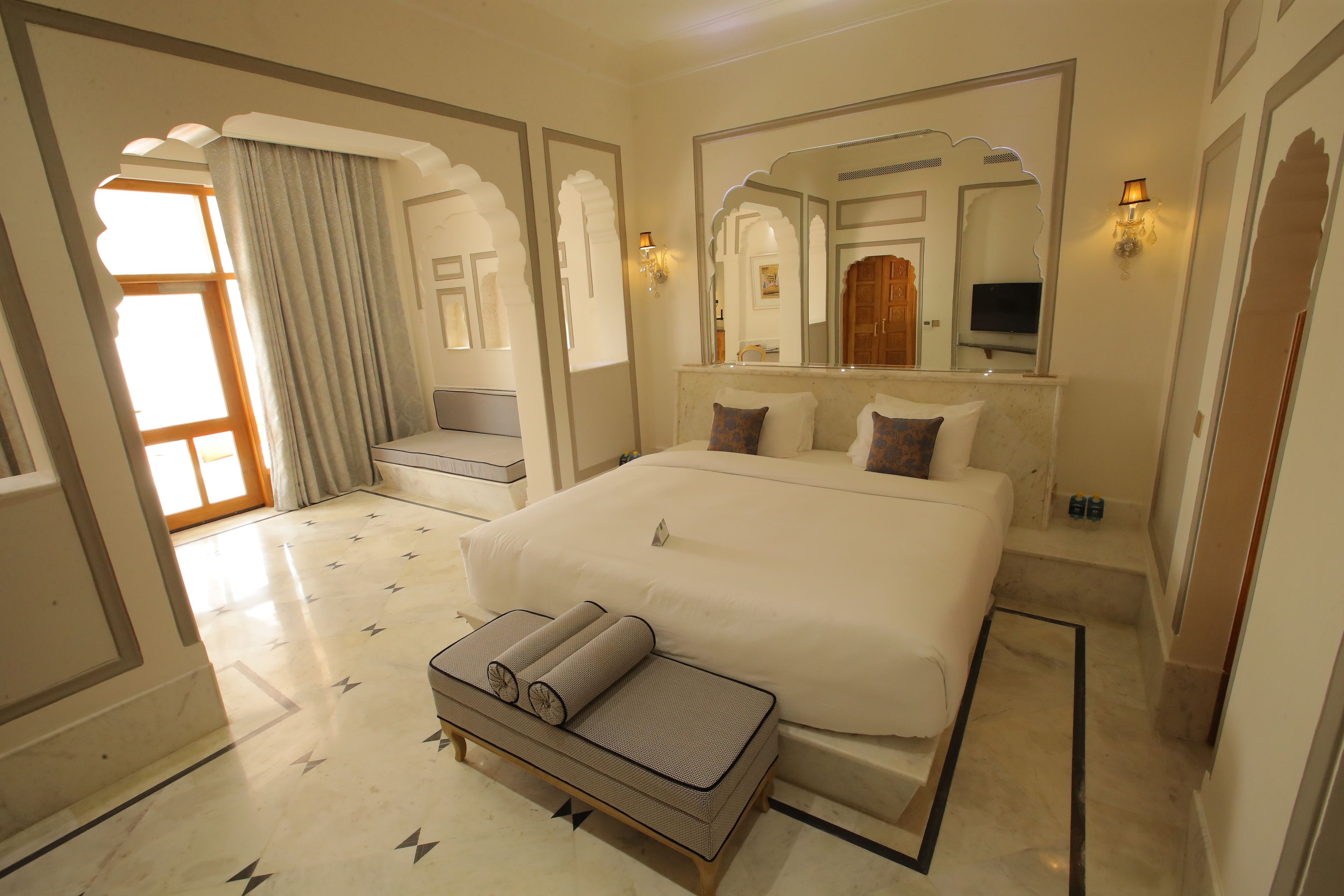 Une chambre spacieuse avec un grand lit, un coin salon comprenant un canapé et des coussins, une petite table et un grand miroir.