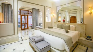 A hotel room with a large bed, a sitting area with a bench, a mirror, and a view of the outside.