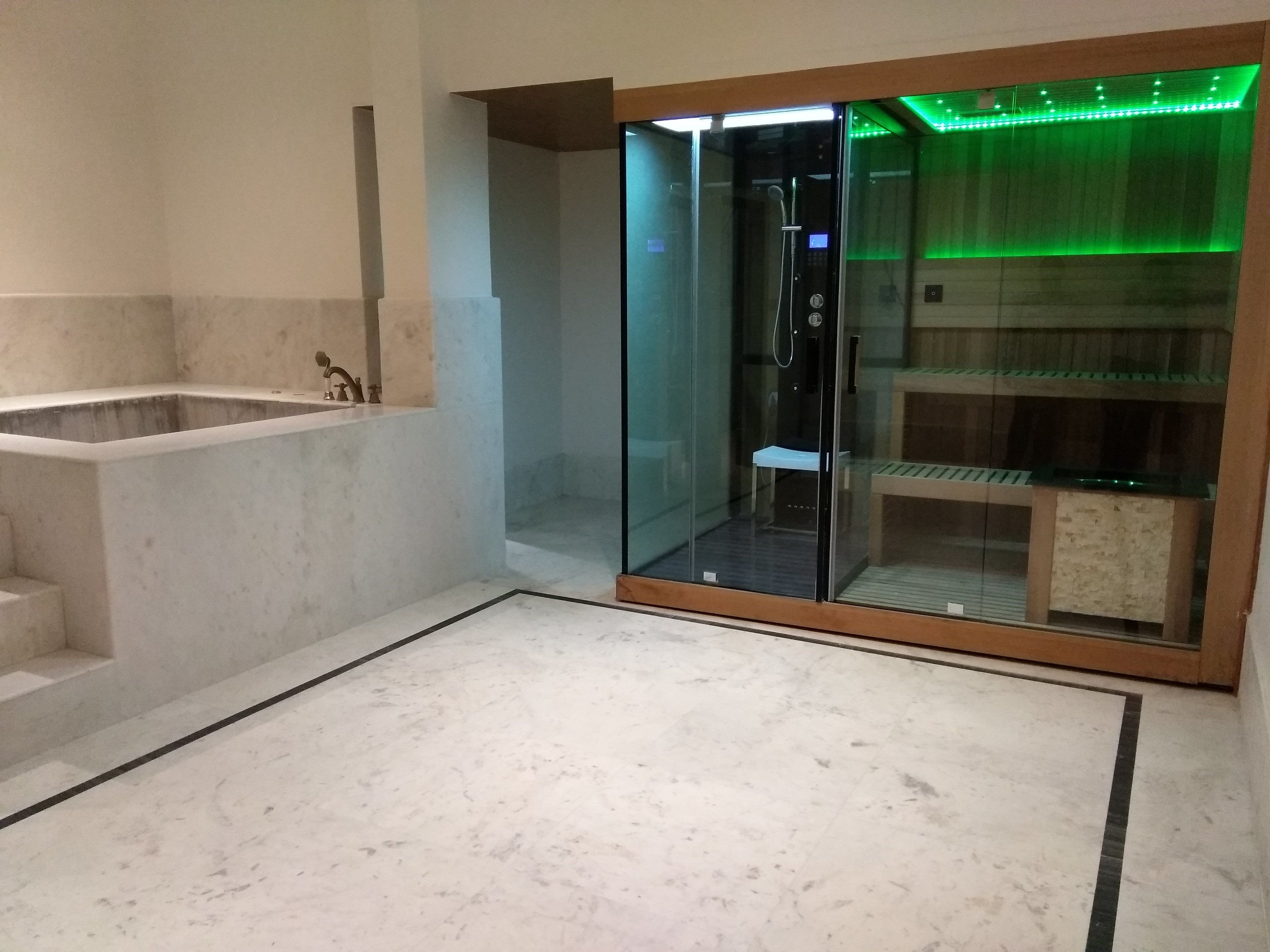 A modern bathroom with a glass-enclosed shower, a bathtub, and a marble floor.