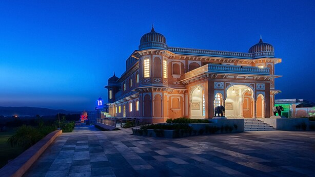 A large, ornate building with multiple domes and arches, featuring a spacious courtyard and a well-lit entrance.