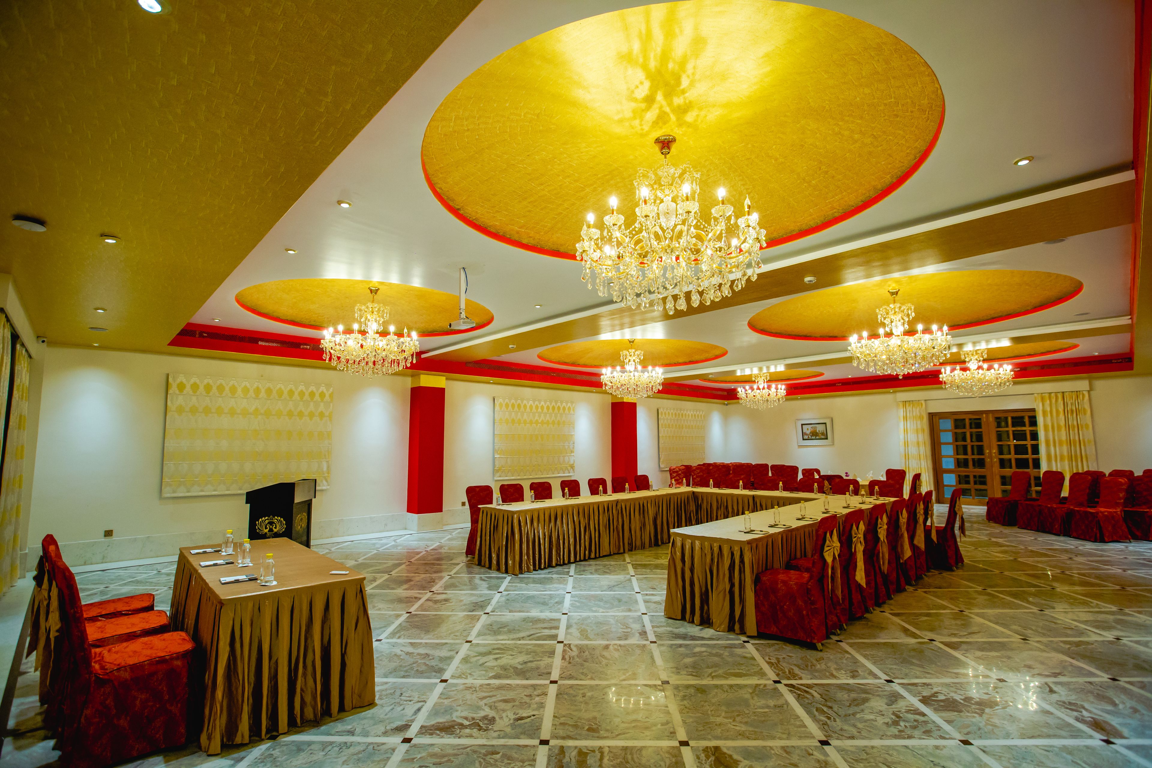 A conference room with multiple tables and chairs, chandeliers, and a marble floor.