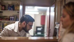 Une personne se tient derrière un comptoir dans une pièce où des étagères sont remplies de divers articles.