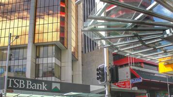 A busy urban street with pedestrians, a TSB Bank building, and a glass structure.