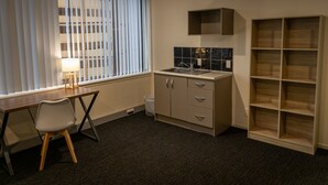 Une petite cuisine équipée comprenant un évier, des placards et une petite fenêtre avec des stores.