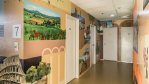 Un couloir orné d’une fresque représentant un paysage, une porte portant l’inscription « 7a » et une autre porte portant l’inscription « 7c ».