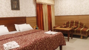 Una habitación de hotel con una cama grande, un cabecero de madera, una mesita con una silla y una cortina.