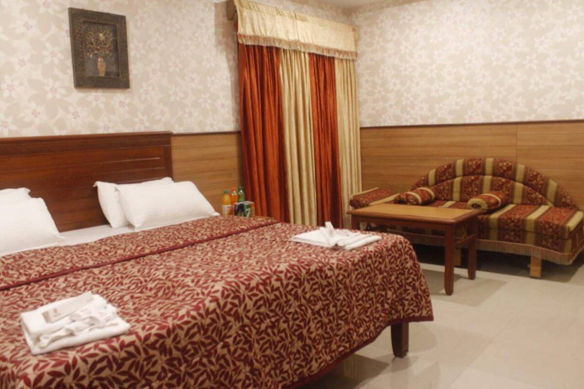 A hotel room with a large bed, a wooden headboard, a small table with a chair, and a curtain.