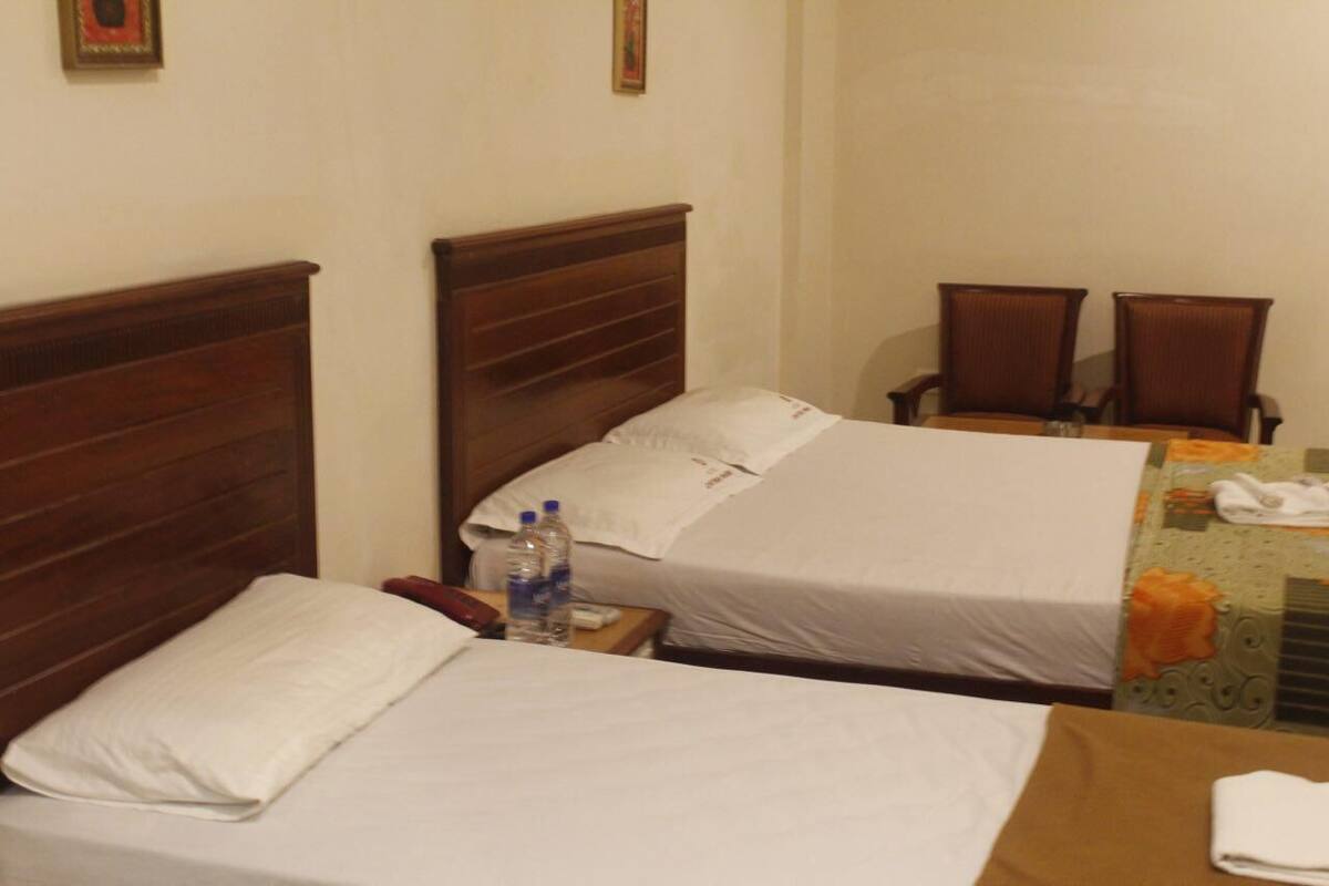 A hotel room with two single beds, a wooden headboard, a small table with a telephone and water bottles, and two chairs.
