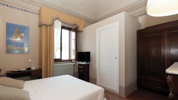 A hotel room with a bed, a television, a desk with a lamp, a wardrobe, and a radiator.