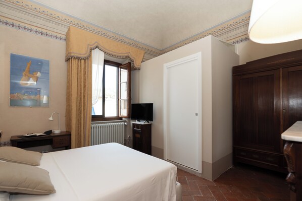 Habitación de hotel con cama, televisión, escritorio con lámpara, armario y radiador.