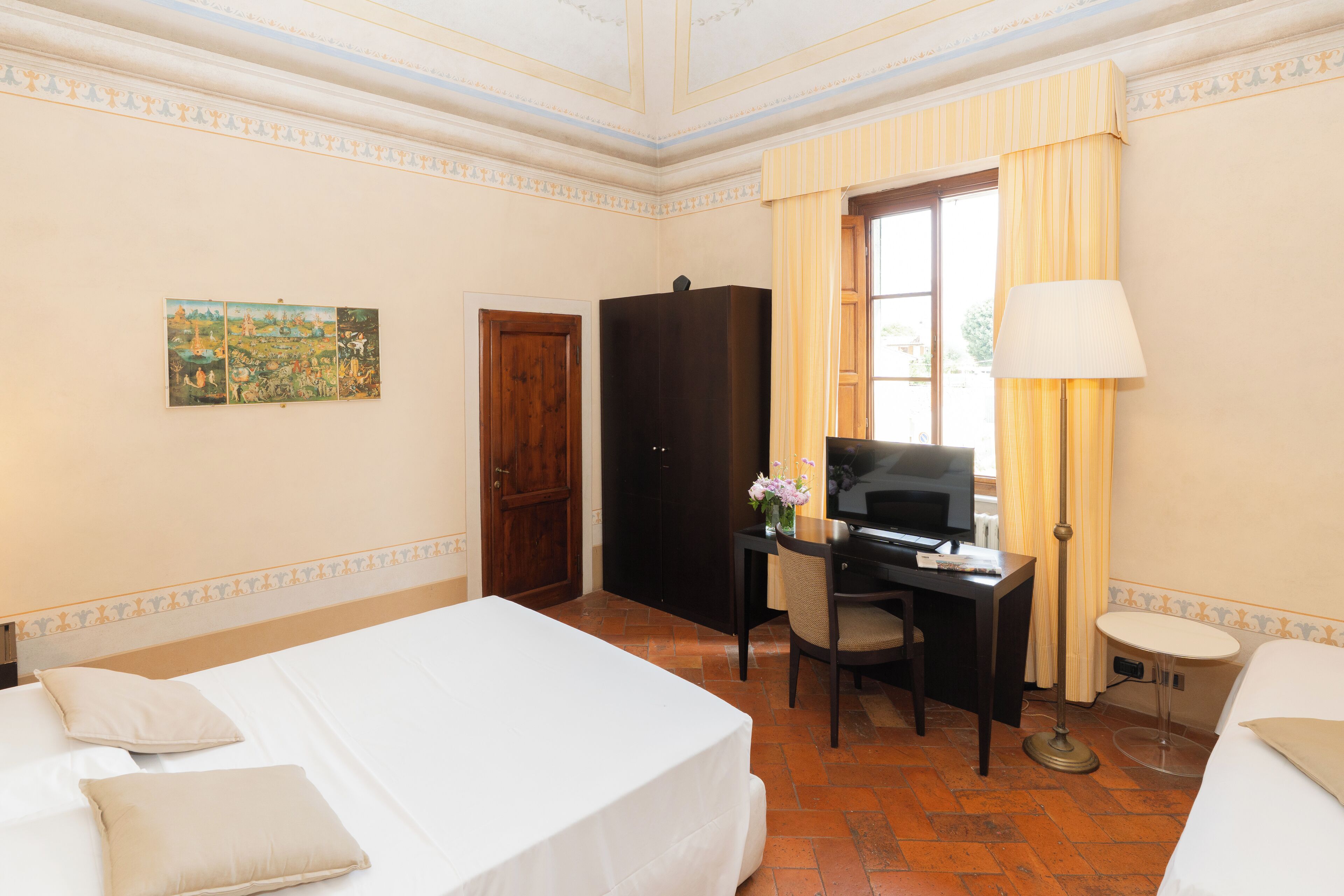 Habitación de hotel con cama, escritorio, silla, televisor y un cuadro en la pared.