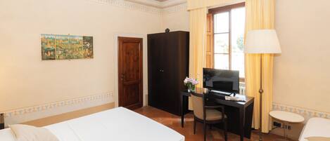 Habitación de hotel con cama, escritorio, silla, televisor y un cuadro en la pared.
