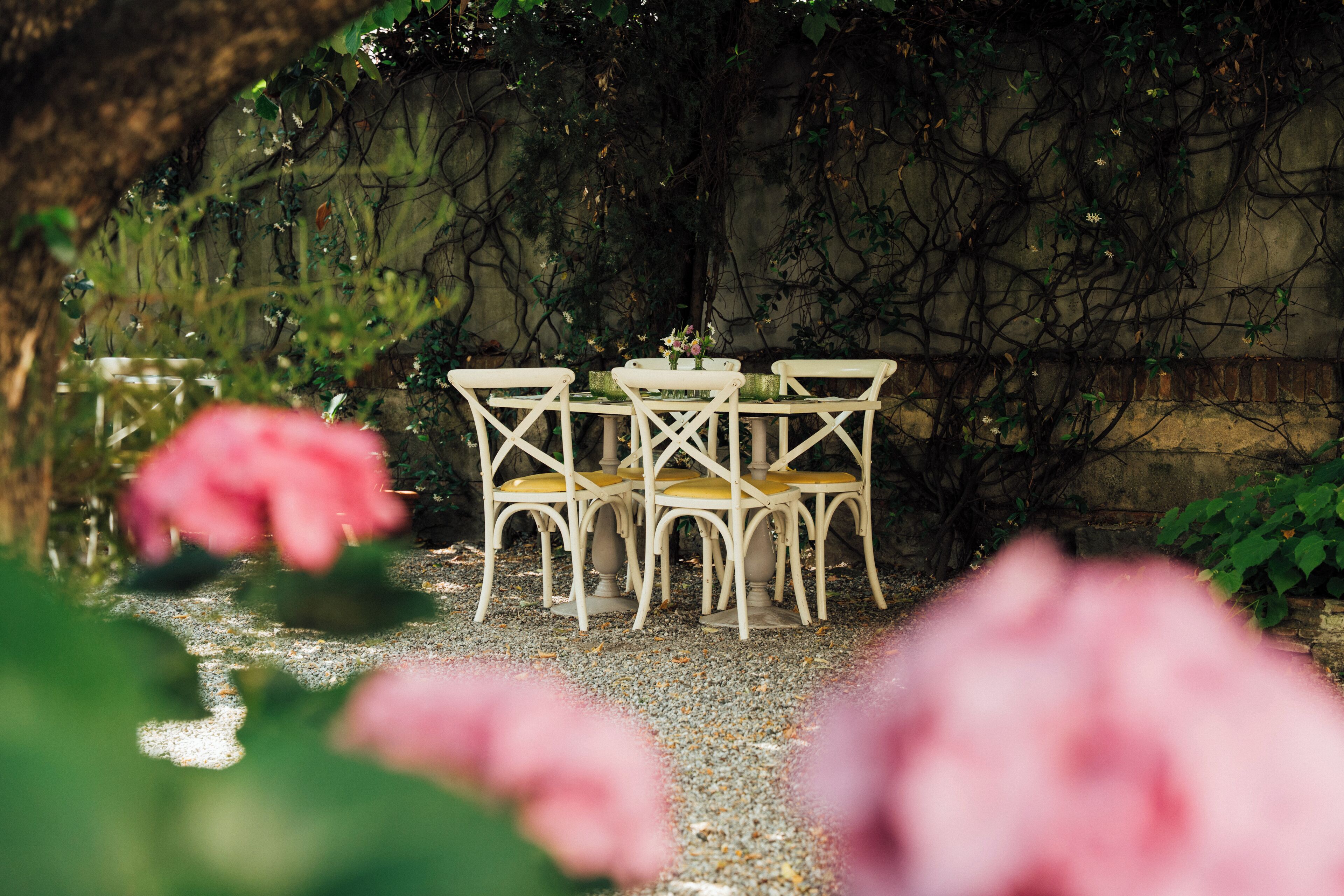 A garden setting with a table and chairs, surrounded by greenery and a stone wall.