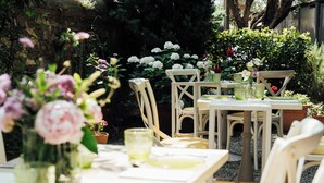 An outdoor dining area with tables and chairs, surrounded by lush greenery and flowers. - B&B VillAmorosa (Vicopisano)