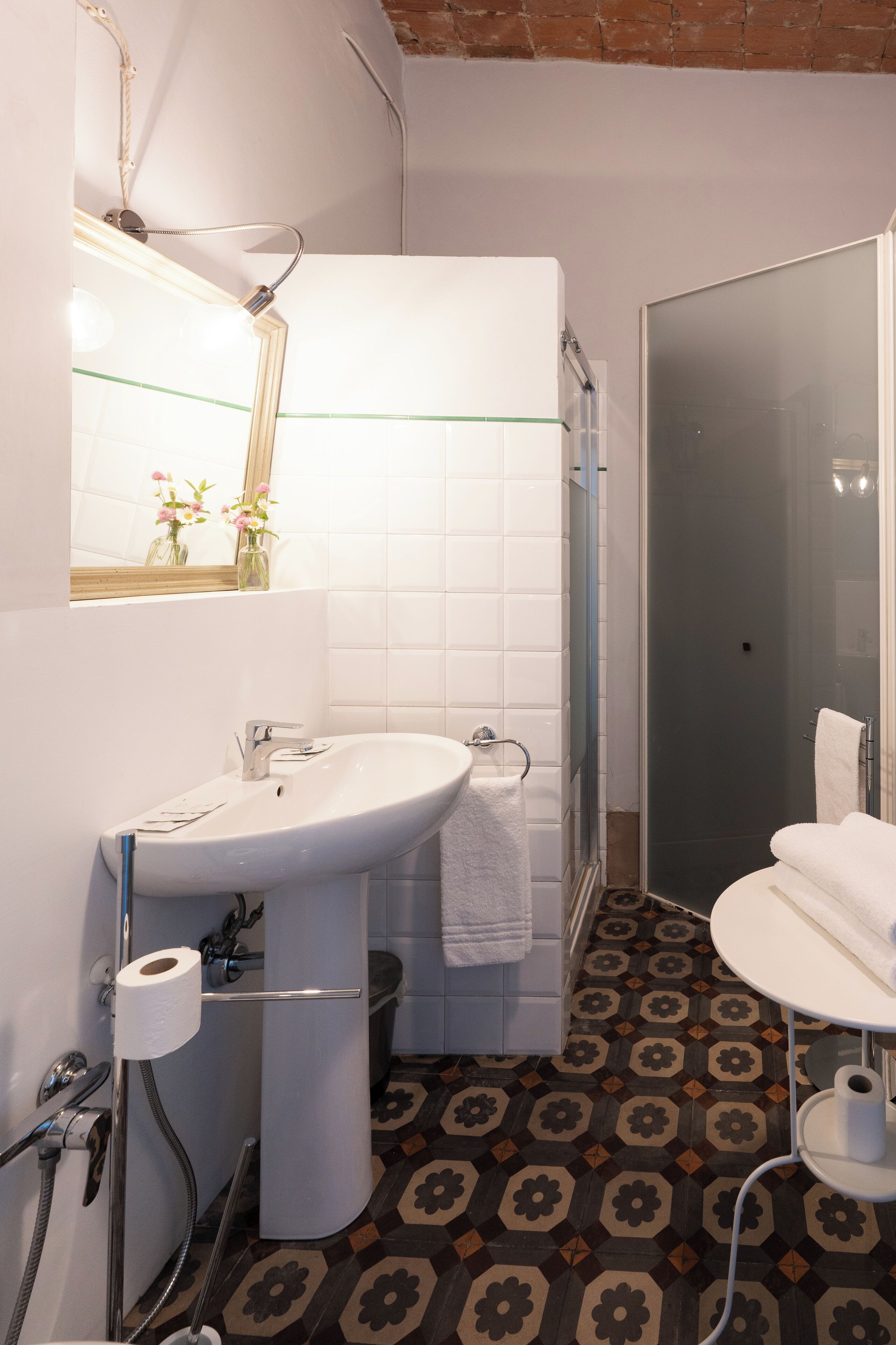 A bathroom with a white sink, toilet, and shower. The floor has a patterned tile design.